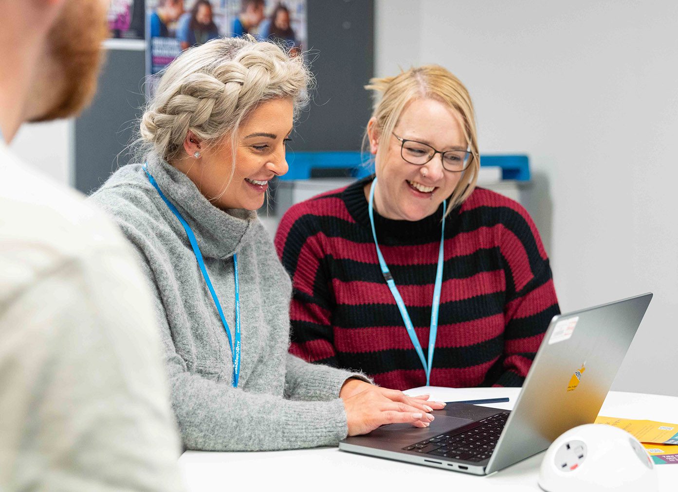 Two students smiling whilst using laptop